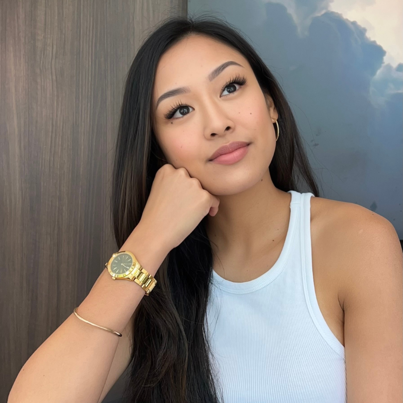 Woman sitting down with fist to her chin wearing a gold watch.