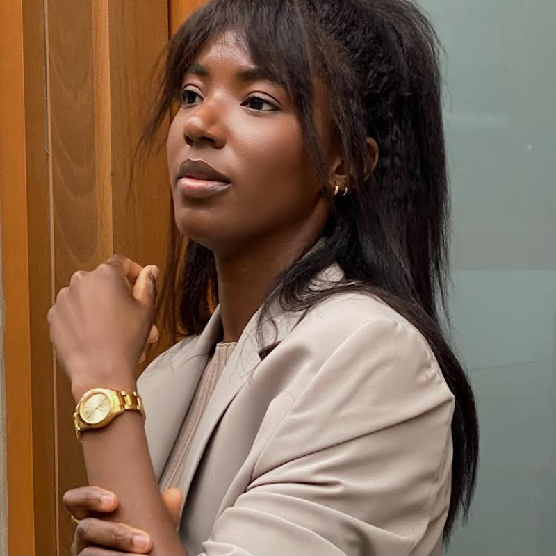 black woman in tan jacket wearing a gold watch