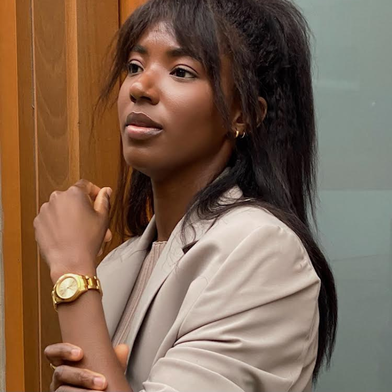 black woman in tan jacket wearing a gold watch 